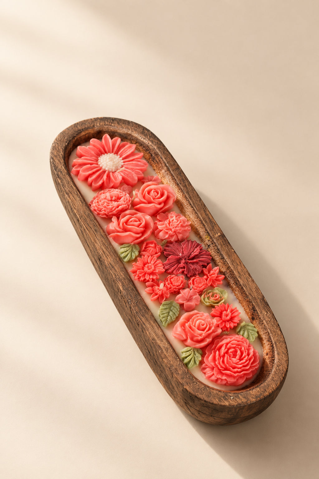 Several elongated wooden trays containing colorful decorative items, including pink and coral flowers, green leaves, shells, and small pearl-like beads, arranged on top of newspaper.