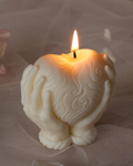 Decorative candle with hands holding a heart design, lit on a soft background