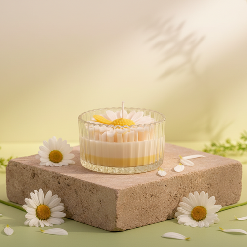 Candle with a daisy design in a glass holder on a soft fabric background