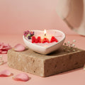 Heart-shaped candle with 'Maa' in red letters and floral decorations, surrounded by string lights on a white surface.