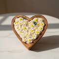 Heart-shaped cookie with floral design held by a hand wearing a gold watch.